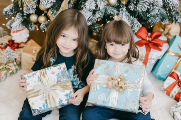 Two young girls joyfully holding beautifully wrapped Christmas gifts in front of a decorated...