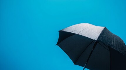 A black umbrella is tilted upward, showcasing its design against a vibrant blue sky. The sunlight enhances the umbrella's features, creating an interesting contrast