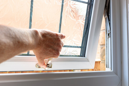 Home owner seen opening a newly fitted PVC double glazed window in a bathroom. Note the frosted leaded glass on the replacement window.