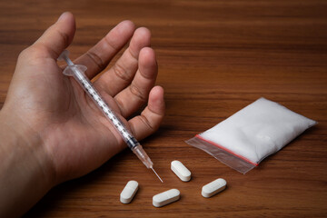 hand trying to reach and use drugs on white table with wooden, methamphetamine, and pills. The concept for drugs addiction, International Day against Drug Abuse. say no to drugs