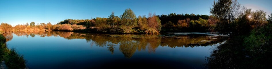 Fototapeta premium Autumn panorama on the lake. Autumn lake in the autumn forest. The autumn leaves of the trees are reflected in the water of the lake
