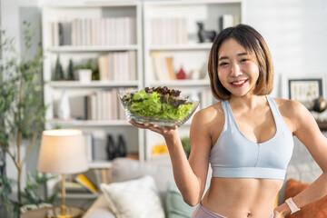 Healthy asian woman in sportswear holding fresh salad bowl at home, fitness lifestyle, healthy eating, balanced diet, wellness and nutrition concept, smiling woman enjoy healthy salad in living room