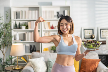 Healthy asian woman in sportswear holding fresh salad bowl at home, fitness lifestyle, healthy eating, balanced diet, wellness and nutrition concept, smiling woman enjoy healthy salad in living room