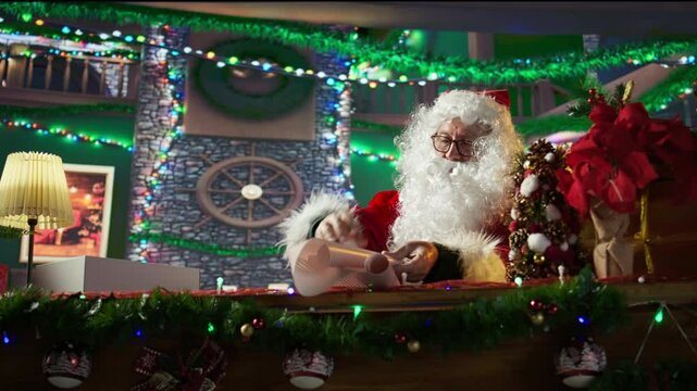 Santa Claus wraps a festive gift box by the fire in his North Pole workshop, surrounded by holiday decorations. Father Christmas prepares gifts and surprises for winter celebration. Camera B.