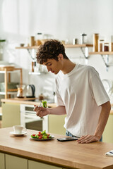 A handsome young man in a stylish kitchen carefully assembles a vibrant salad while enjoying a peaceful morning.