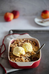Crumble, Crisp or Cobbler with nectarines, peaches, rolled oats and scoop of ice cream in casserole dish on a metal tray. American cuisine. Easy dessert.