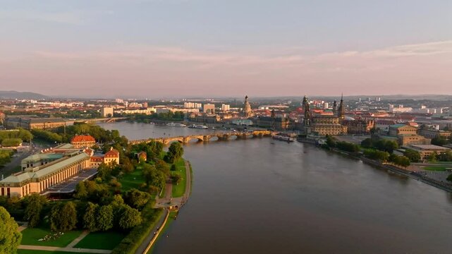 Drone video of Dresden during a flood with warm light illuminating the scene. A tram crosses a bridge, while the damaged Carola Bridge is visible in the background. Drone move forward.