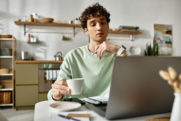 Curly-haired man sips coffee thoughtfully while working on his laptop in a contemporary home office.