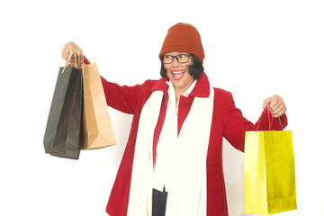 A middle-aged woman wearing a red overcoat and a beanie is holding several shopping bags