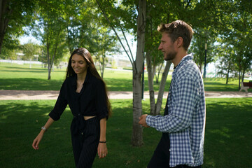 Naklejka premium A couple shares a joyful laugh outdoors, basking in the warmth of the sun while playfully interacting beneath leafy trees in a vibrant park setting