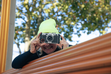 Woman in yellow beanie using vintage camera outdoors in autumn