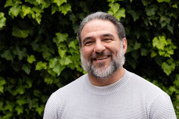 Smiling mature man outdoors, enjoying nature with lush green leaves in background