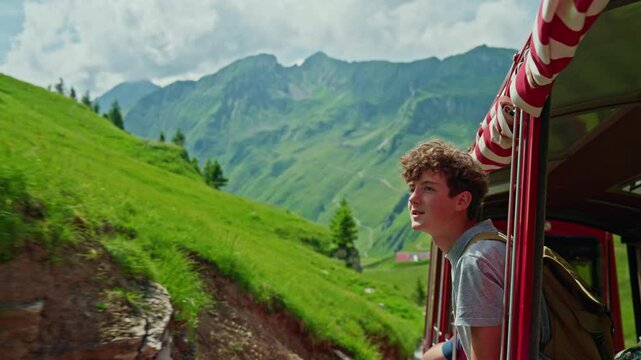 Portrait of young guy, teenager travels through Switzerland riding tourist red train enjoying views of alpine meadows and alpine mountains, Brienz