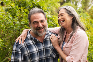 Happy mature couple laughing together in lush garden, enjoying outdoor moments