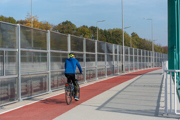 Cyclist enjoying a clear autumn day while riding on marked bike path, wearing safety helmet for protection. Concept of outdoor recreation, active lifestyle, and safe cycling practices in nature. 