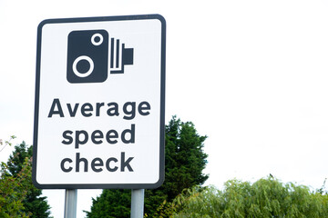 Large roadside sign notifying motorists, that the stretch of highway ahead is an Average Speed Check zone. Low view of sign against a clear sky with green bushes nearby.