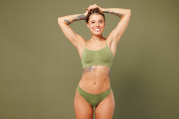 Fototapeta premium Young smiling happy nice lady woman with slim skinny body perfect skin she wear top bra lingerie stand hold hair raise up hands isolated on plain pastel green background. Lifestyle diet fit concept.