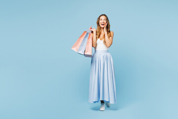 Full body young shocked surprised woman wear casual clothes hold paper package bags after shopping spread hand look camera isolated on plain light blue background. Black Friday sale buy day concept.