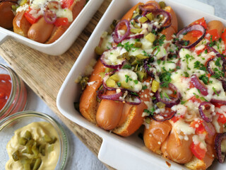 Baked Hot Dogs with Melted Cheese, Red Onions, Tomatoes,  and Pickles in Baking Dish