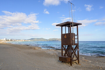 A rustic lifeguard tower stands on a beach overlooking the ocean and distant mountains, mallorca balearic islands, spain