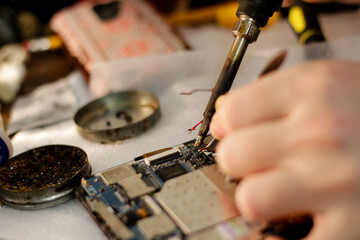 A close-up image of a skilled technician using a soldering iron to repair a smartphone, showcasing...