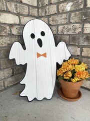 Halloween ghost on a front porch with flowers and a brown brick wall in the background.
