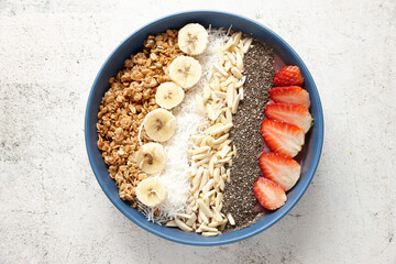 A blue bowl with sliced bananas, strawberries, granola, chia seeds, desiccated coconut and almonds