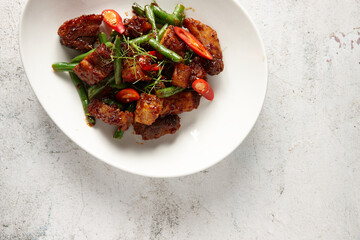 Braised caramel chicken in a bowl topped with red chili slices, herb, and long beans