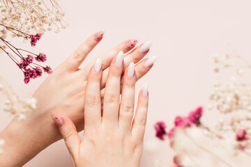 Spring manicure of woman hands with white gel polish and dried flower design. Female hands and dried gypsophila flowers bleached on a beige background.