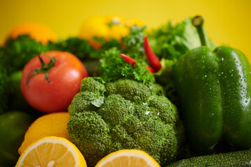 Assorted vibrant vegetables and fruits arranged creatively against a yellow background, showcasing fresh produce including broccoli, lemon, tomato, and peppers