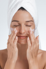 Close-up of a woman with her eyes closed, enjoying a calming skincare routine as she applies face cream. Ideal for promoting beauty, skincare, relaxation, and self-care products in wellness campaigns.