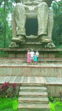 A cheerful family poses in front of a large statue amidst the lush, green rice terraces of Ubud, Tegalalang.