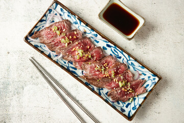 rectangular plate with thin slices of rarely cooked beef topped with green onions