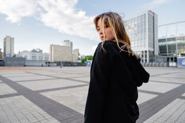 Young woman in black hoodie walking in urban area during sunset