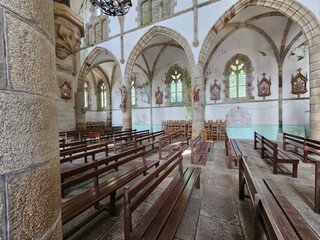 Des rangées de bancs en bois remplissent l'intérieur de l'église, entourées par des murs en pierre ornés de statues et de stations du chemin de croix, avec de grandes arches et des vitraux