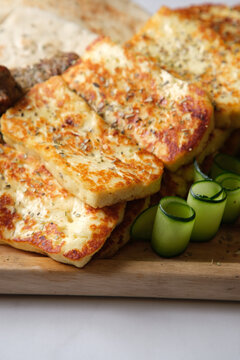 Closeup of seared halloumi cheese with thin slices of cucumber rolled up served on a wooden board