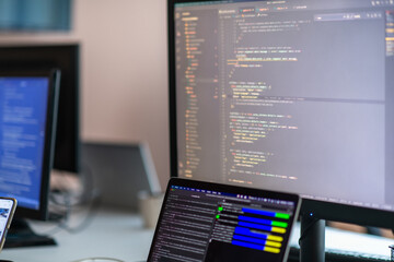 Computer screens running programming code in empty software developing agency office and computers parsing data algorithms in background. Neural network servers cloud computing in data room.