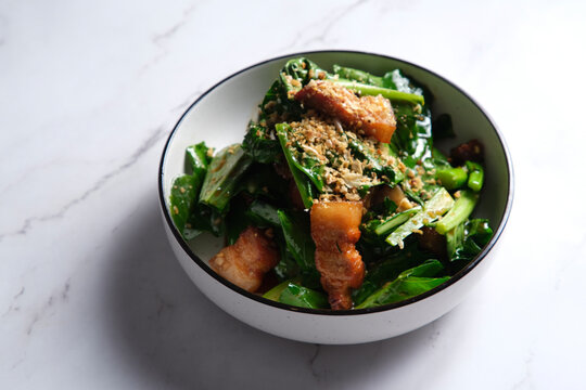 Stir-fried green leafy vegetable with pork belly slices garnished with crushed peanuts.