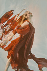 Girl in red dress with long hair swims underwater on light background