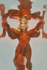 Girl in red dress with long hair swims underwater on light background