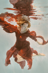 Girl in red dress with long hair swims underwater on light background