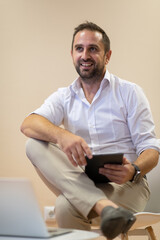 A confident businessman sitting and using laptop with a determined expression, while a beige background enhances the professional atmosphere, showcasing his productivity and expertise.