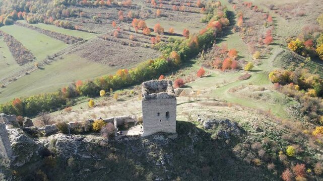 A breathtaking view of the remnants of a medieval tower perched atop a hill, surrounded by vibrant autumn foliage and rolling green hills. A tranquil setting for history enthusiasts.Cetatea Trascăului