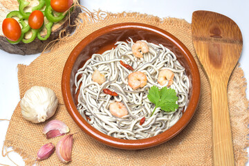 Eels with garlic prawns in a clay pot with garlic cloves, a coriander leaf, vegetables and wooden spoon on a white background