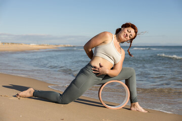 Early morning beach stretch: woman in low lunge pose with yoga wheel
