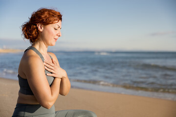 Obraz premium Red-haired woman sitting on the sand doing meditation early in the morning