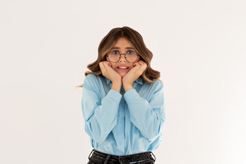 Anxiety - young woman with glasses wearing blue shirt over white background covering her chin with hands scared from something or someone bitting nails.