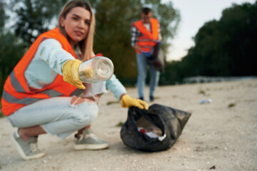 Picking up the bottle. A volunteers collects garbage on a muddy beach
