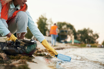 Picking bottle from the water. A volunteers collects garbage on a muddy beach