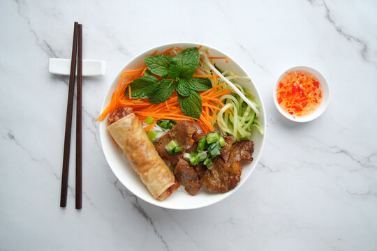 Beef noodle salad topped with fried lumpia with salad dressing next to it.